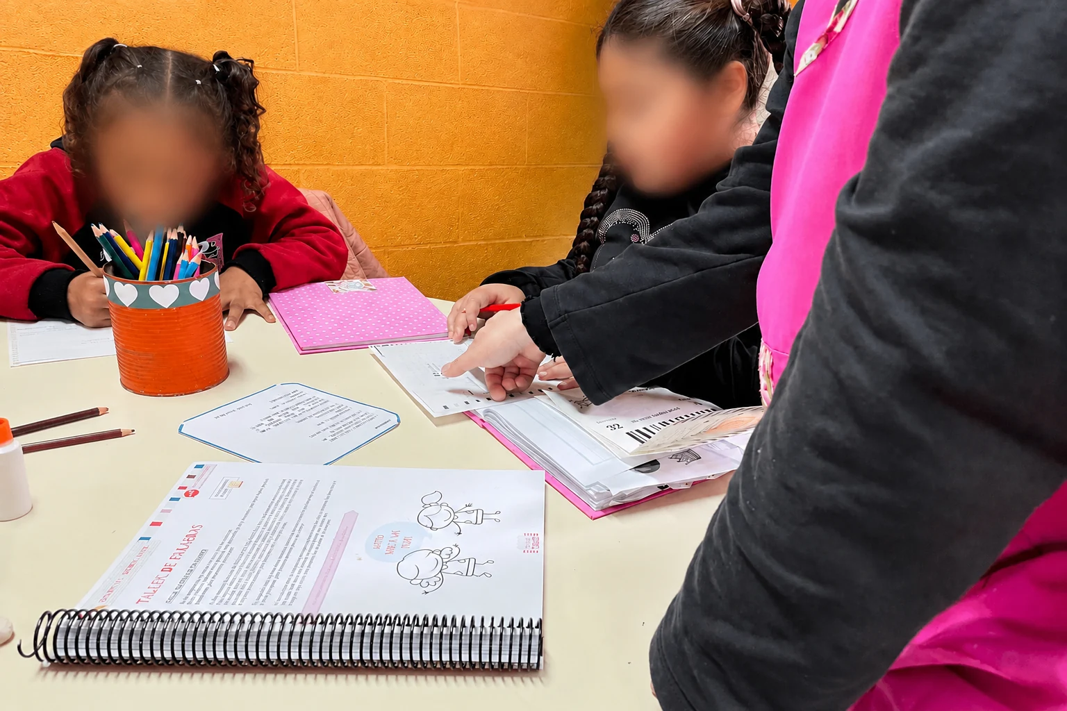 Una docente acompaña a una alumna señalando una consigna en el libro